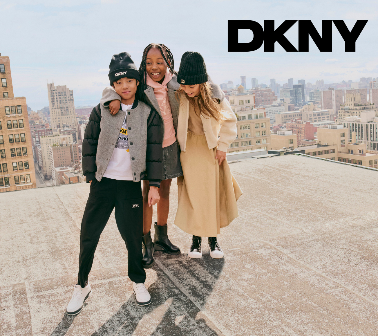 Three kids  posing on a rooftop with a cityscape background and DKNY branding.