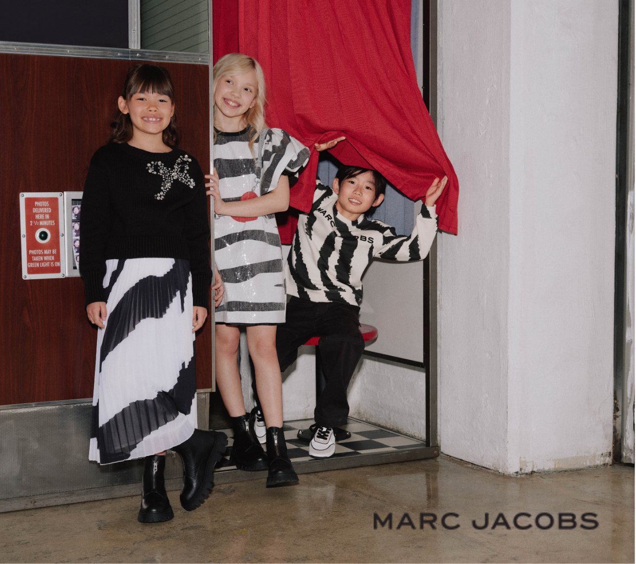 Three children in stylish outfits standing in a doorway with 'Marc Jacobs' branding.