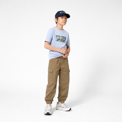 Person wearing a light blue t-shirt with text, beige cargo pants, and a navy cap on a white background